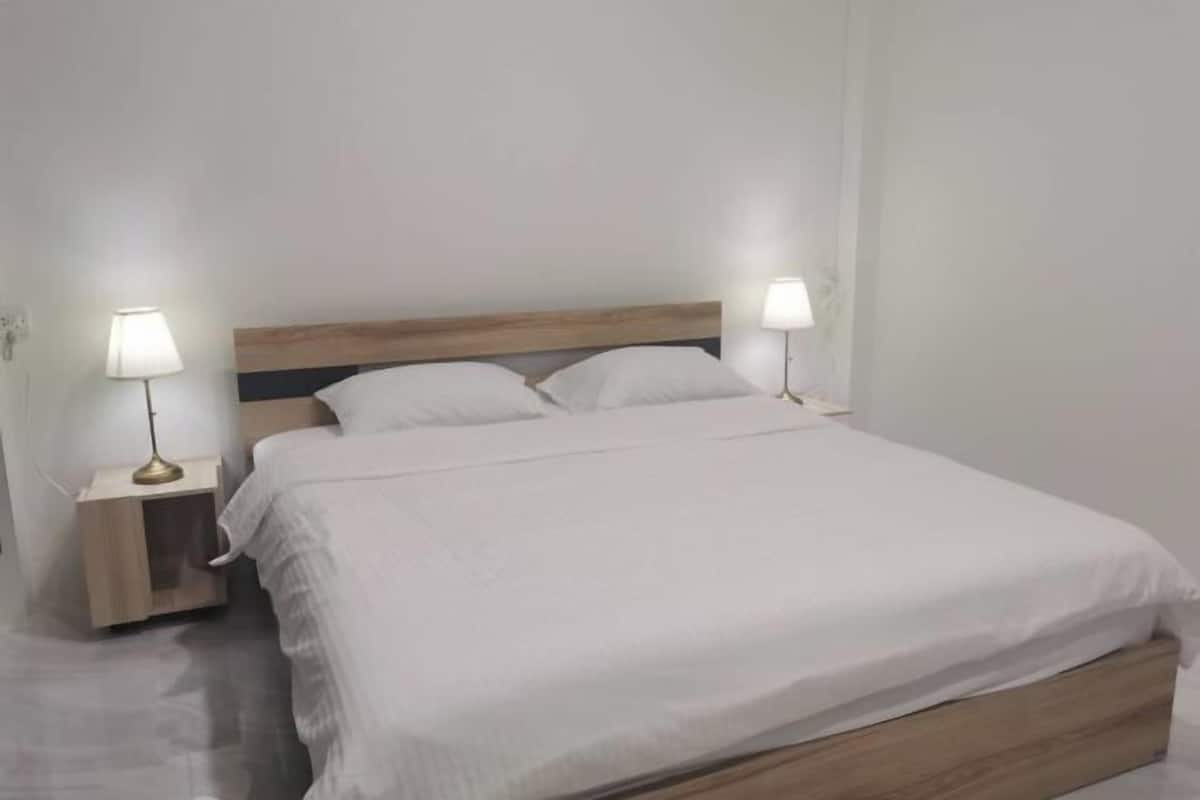 A single bed with a wooden headboard, two bedside lamps, and a white bedspread.