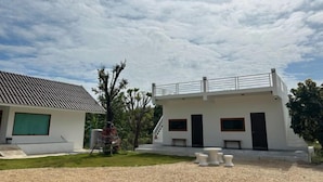 Une maison moderne à deux étages, dotée d’un toit plat, d’un balcon et d’un petit patio aménagé avec du mobilier d’extérieur.