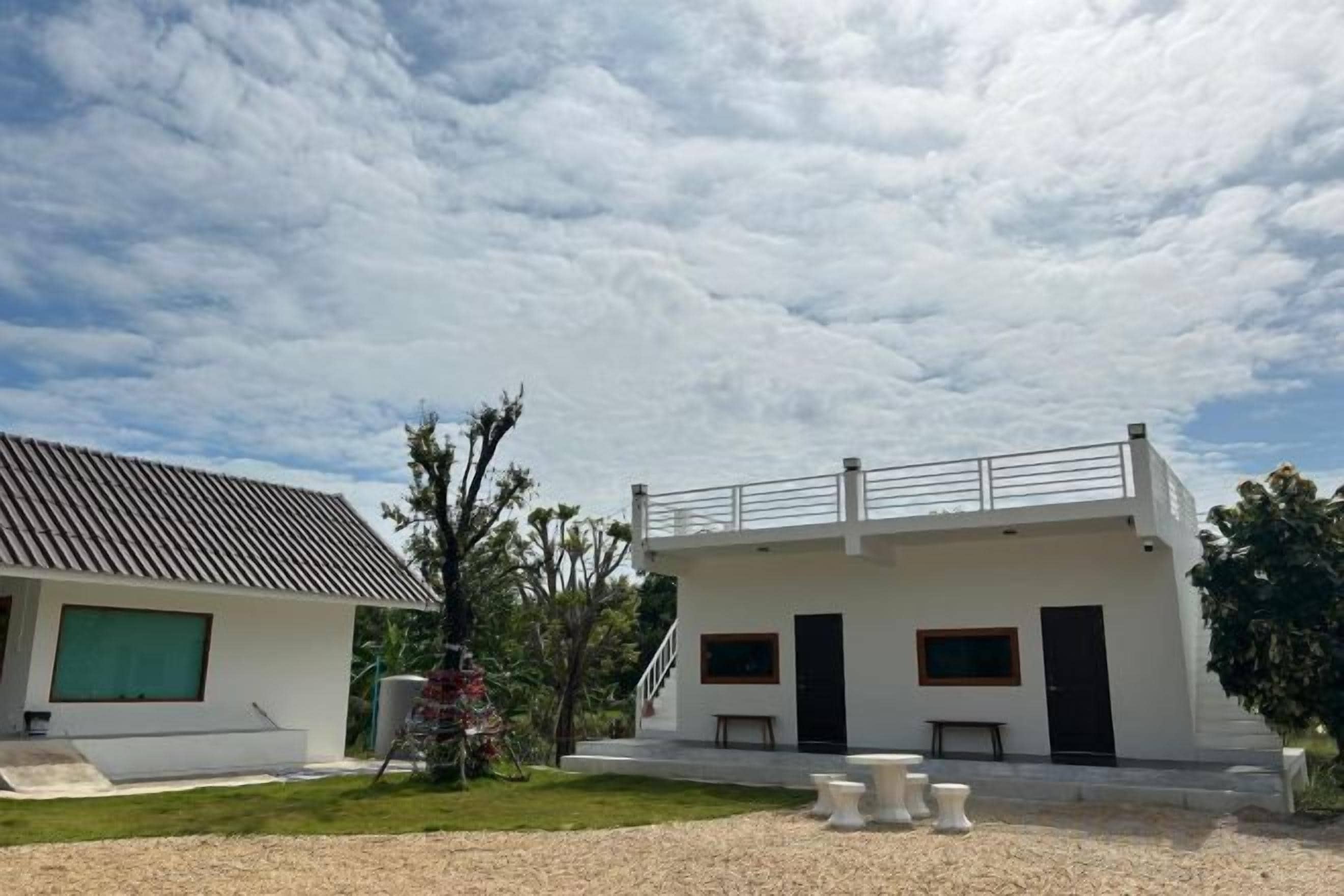 A modern two-story building with a flat roof, a covered outdoor seating area, and a gravel driveway.