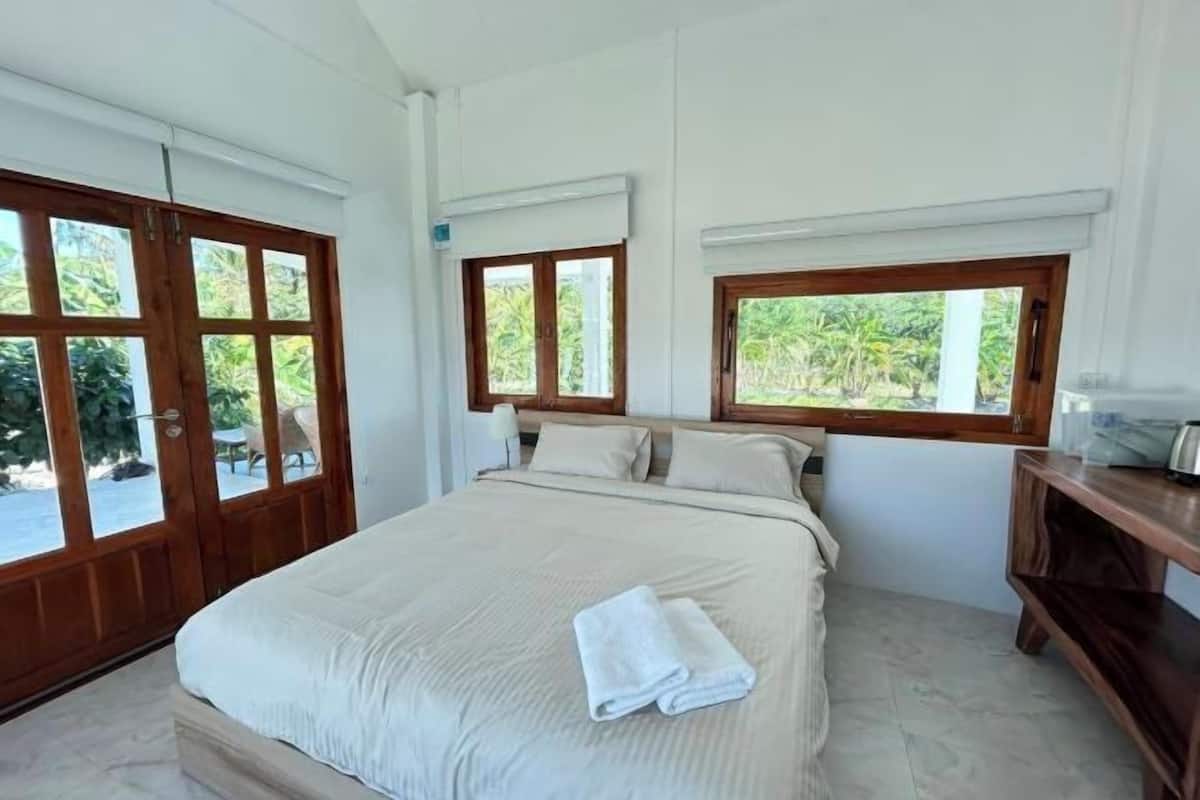 A bedroom with a bed, a window, and a wooden nightstand.