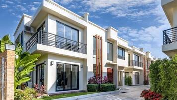A modern multi-story residential building with balconies, large windows, and a well-maintained garden.