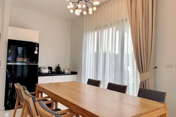 A modern kitchen with a black refrigerator, a wooden dining table with four chairs, and a large window with sheer curtains. - Hideaway Lake Villas (Phuket)
