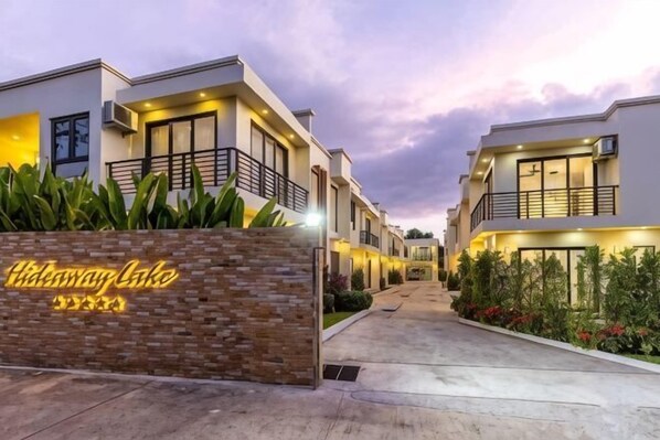 A modern hotel with a brick entrance sign, multiple balconies, and a well-lit pathway. - Hideaway Lake Villas (Phuket)