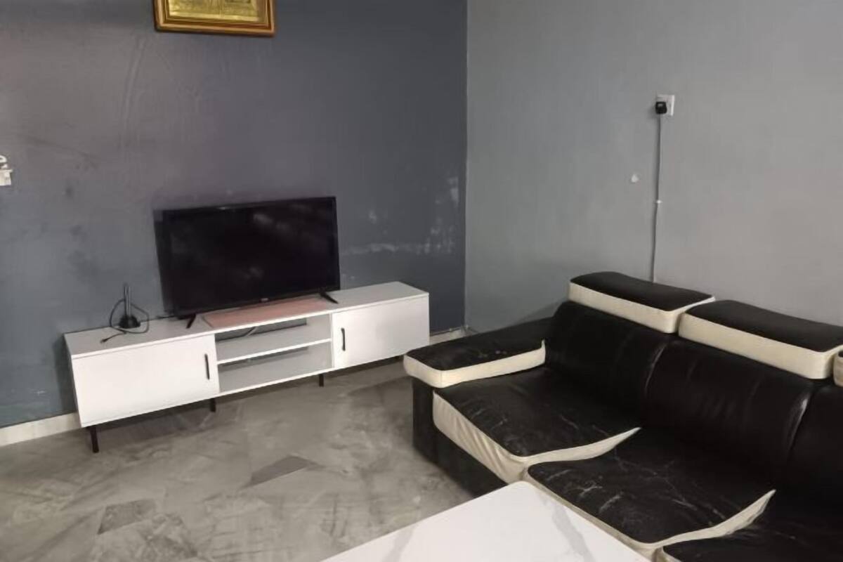 A living room with a black leather sofa, a white entertainment unit, and a flat-screen TV.