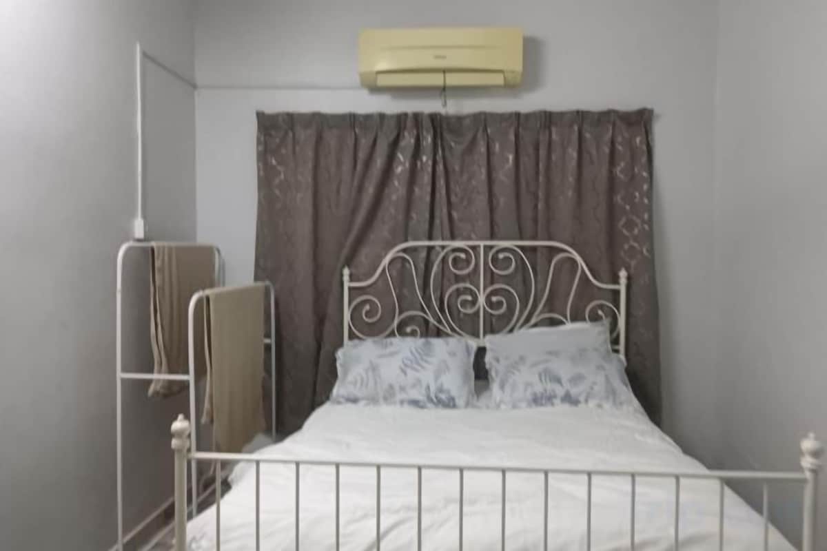 A single bed with a metal frame, a plain wall, and a curtain.