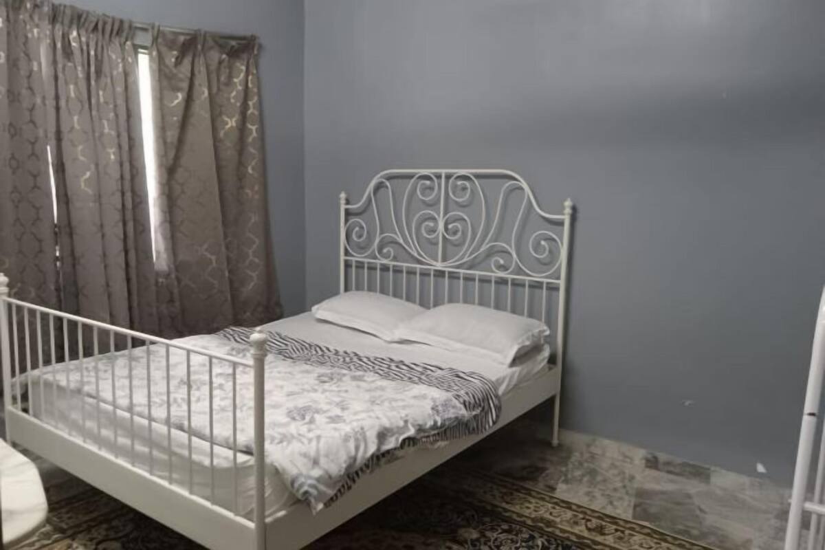 A single bed with a metal frame, white bedding, and a patterned throw.