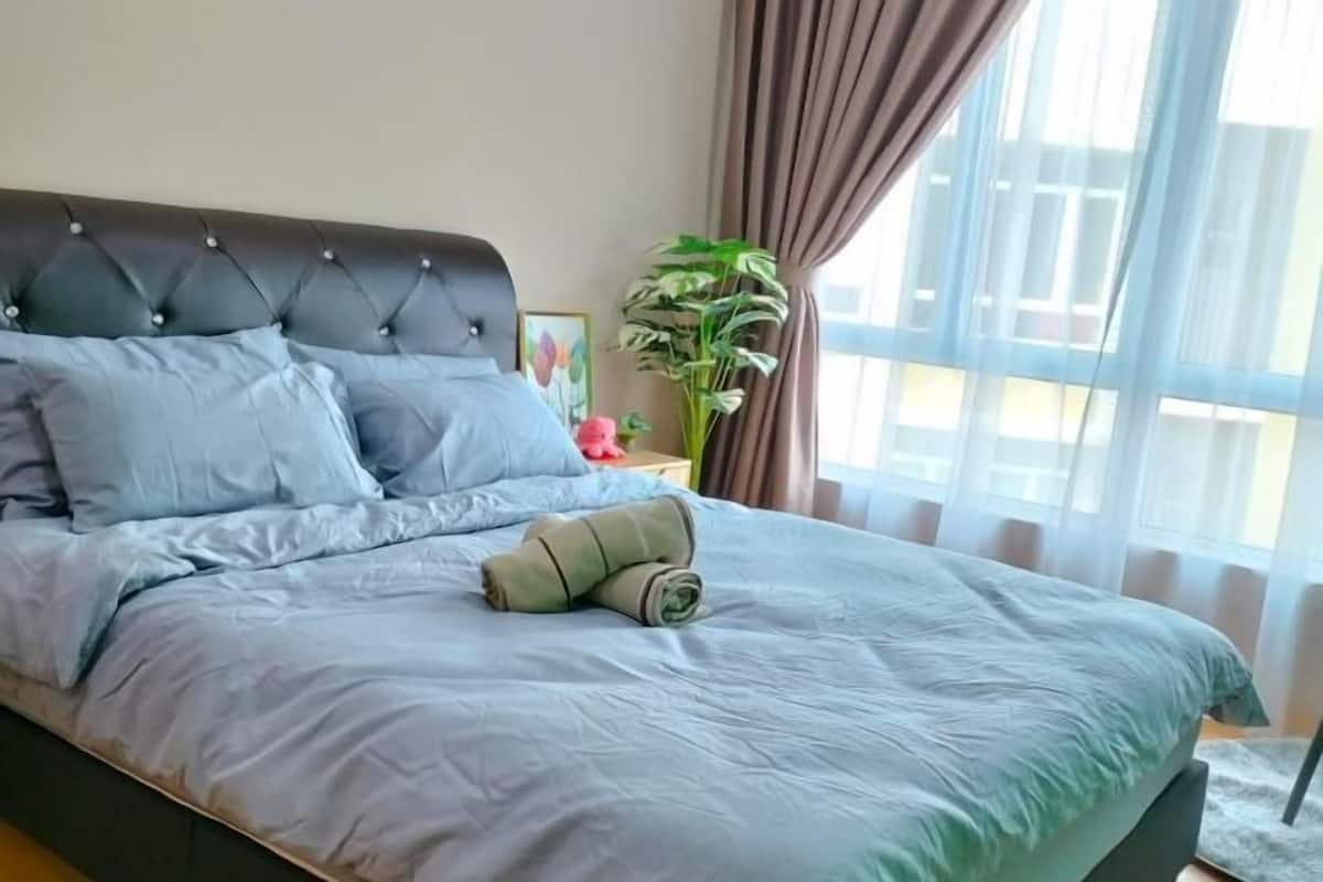 A neatly made bed with a tufted headboard, a potted plant, and a window with curtains.