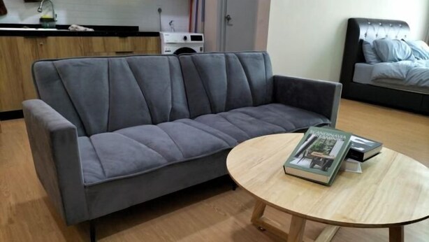 A modern living room with a grey sofa, a round wooden coffee table, and a bed with a headboard in the background. - Mahkota Valley Suite Indera Mahkota@ Netflix (Kuantan)
