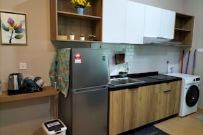 A compact kitchen with a stainless steel refrigerator, a washing machine, wooden cabinets, and a tiled backsplash. - Mahkota Valley Suite Indera Mahkota@ Netflix (Kuantan)