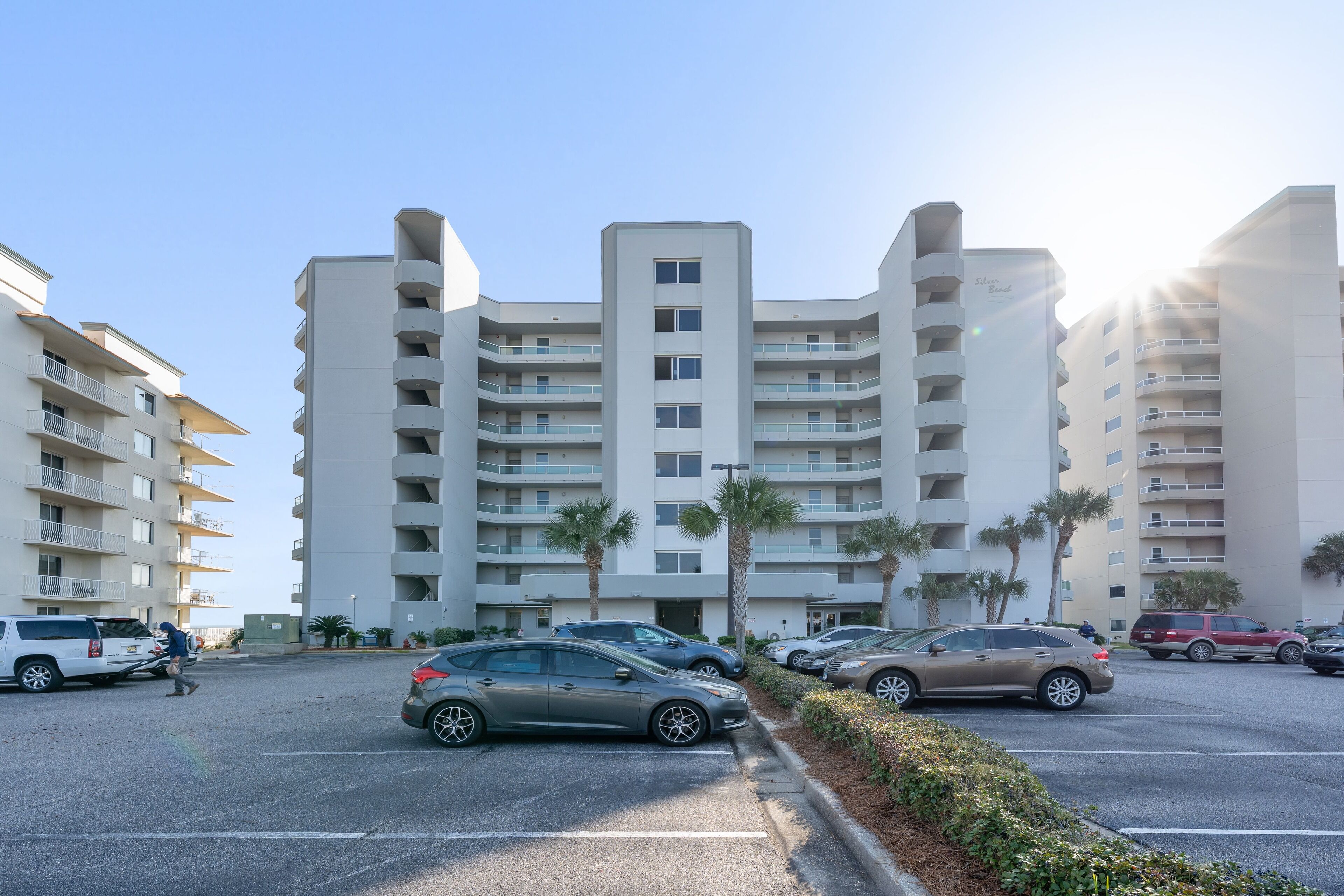 A multi-story parking garage with several cars parked, surrounded by modern buildings with balconies and palm trees.