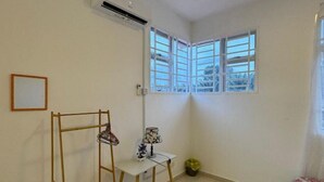 A room with a corner window, a small table with a lamp, a clothes drying rack, and a trash bin. - Fallem's Homestay I 4 Rooms I Fully Aircond I WiFi (Melaka)