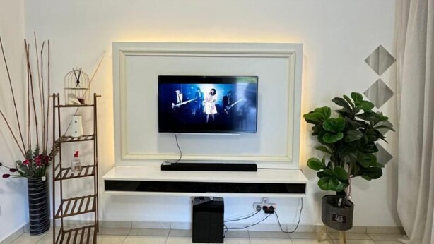A flat-screen TV mounted on a white wall with a shelf below. - Fallem's Homestay I 4 Rooms I Fully Aircond I WiFi (Melaka)