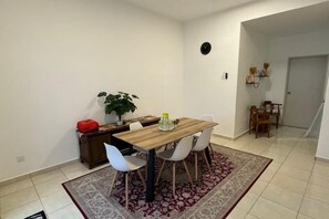 A dining area with a wooden table, white chairs, a patterned rug, a potted plant, and a small red object on the side table. - Fallem's Homestay I 4 Rooms I Fully Aircond I WiFi (Melaka)