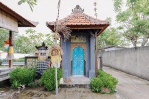A small shrine with a blue door, surrounded by greenery and a concrete wall. - The Lavana Jhonny Kibung Villas Lembongan (Bali)