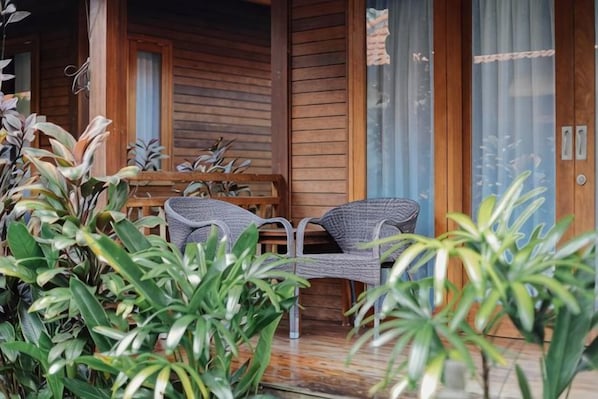 A wooden cabin with a porch, two wicker chairs, and a table.