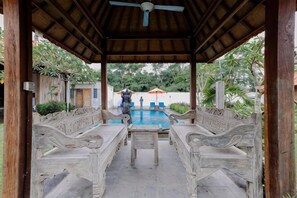 Un espacio al aire libre techado con piscina, bancos y una mesa.