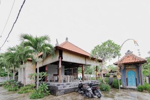 Un petit bâtiment doté d’un toit en tuiles, entouré de verdure et avec une moto garée à proximité.