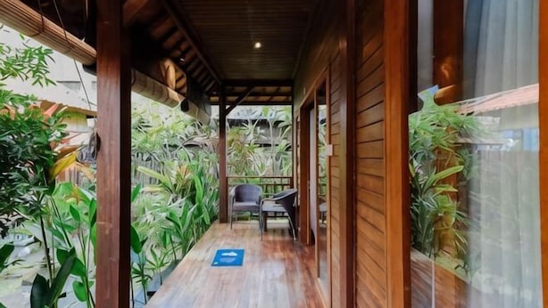 A wooden corridor with a chair, potted plants, and a blue directional sign. - The Lavana Jhonny Kibung Villas Lembongan (Bali)
