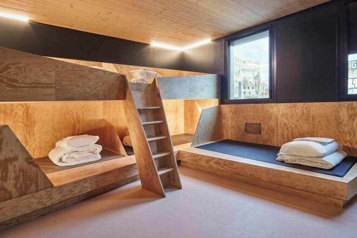Una habitación moderna con literas, una escalera de madera y una ventana con vista a la ciudad.