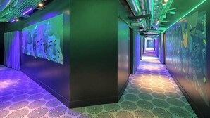 Un couloir doté d’un sol à motifs, d’un éclairage vert et violet, et d’une fresque murale.