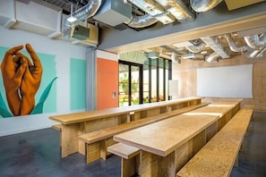 Una sala de conferencias moderna con largas mesas de madera, una gran pizarra blanca y un mural de manos en la pared.