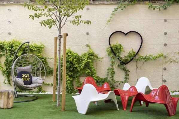 Un'area giardino con una poltrona a dondolo, sedie rosse e bianche e una decorazione a forma di cuore su un muro.