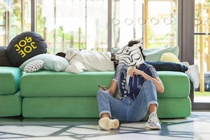A person sitting on a green sofa with a patterned pillow, using a mobile device. - JO&Joe Paris Gentilly - Auberge de Jeunesse (Gentilly)