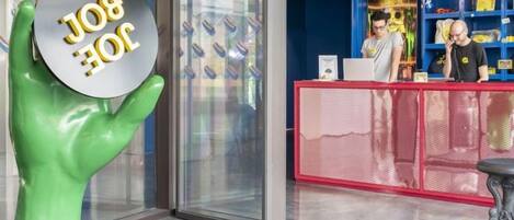 Un área de recepción con puerta de vidrio, una escultura de mano verde y un mostrador rojo.
