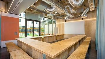 Ein modernes Interieur mit einem langen Holztisch, Bänken, freiliegenden Leitungen und großen Fenstern.