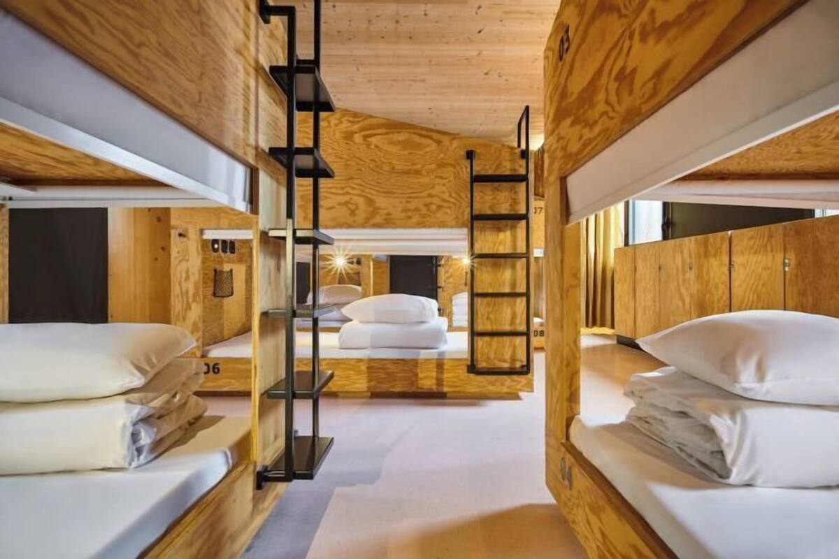 Habitación pequeña con temática de madera, con literas, una escalera y una cama central.