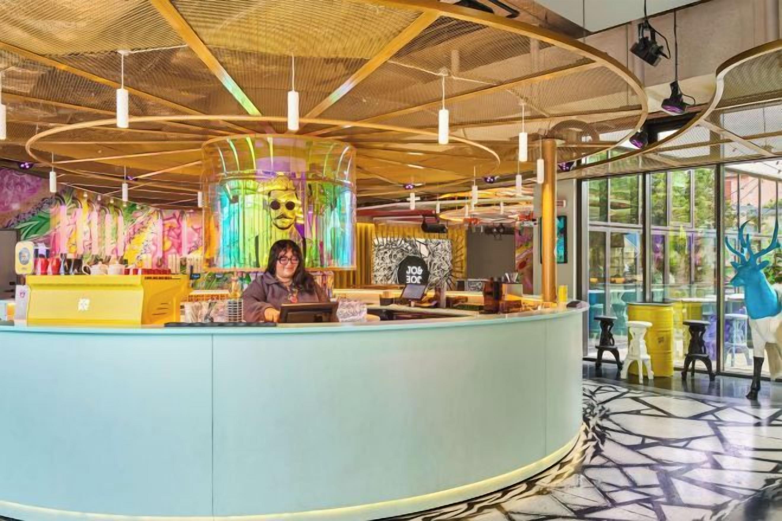 Un intérieur moderne avec un comptoir d’accueil incurvé, un grand écran numérique et un plafond orné de luminaires suspendus.
