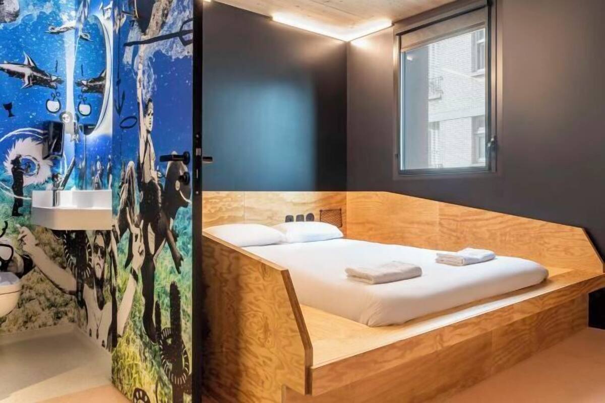 Una habitación moderna con cama, ventana y pared decorada con un mural.