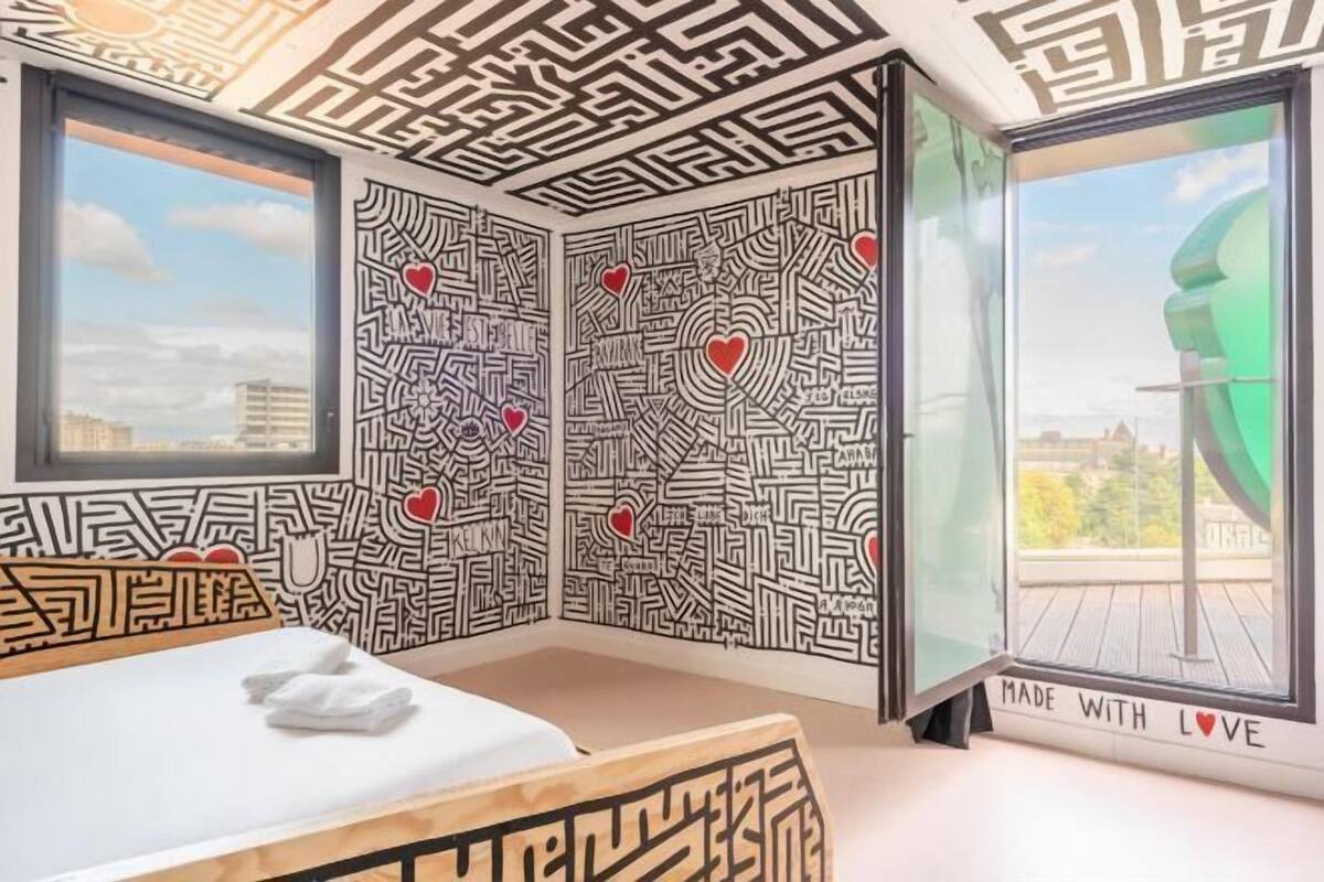 Una habitación con cama, ventana y pared con un diseño laberíntico y corazones.