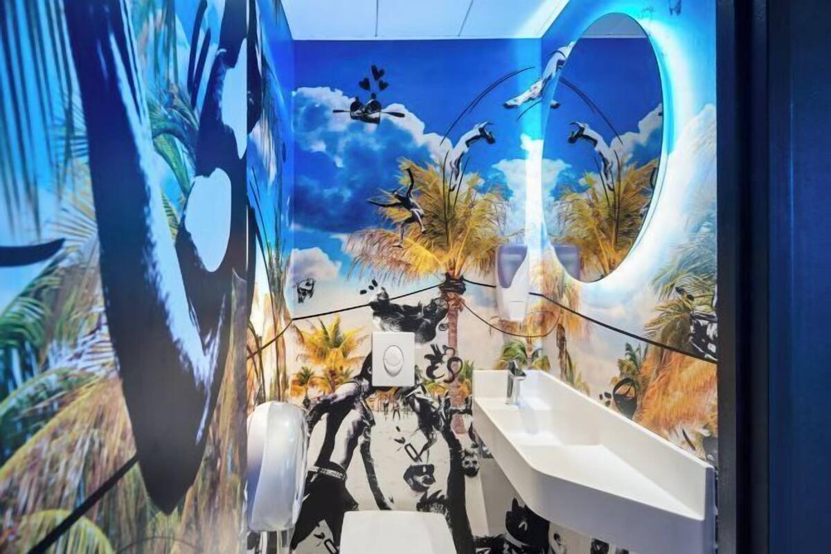 Un baño con un mural de una escena tropical, un lavamanos y un espejo.