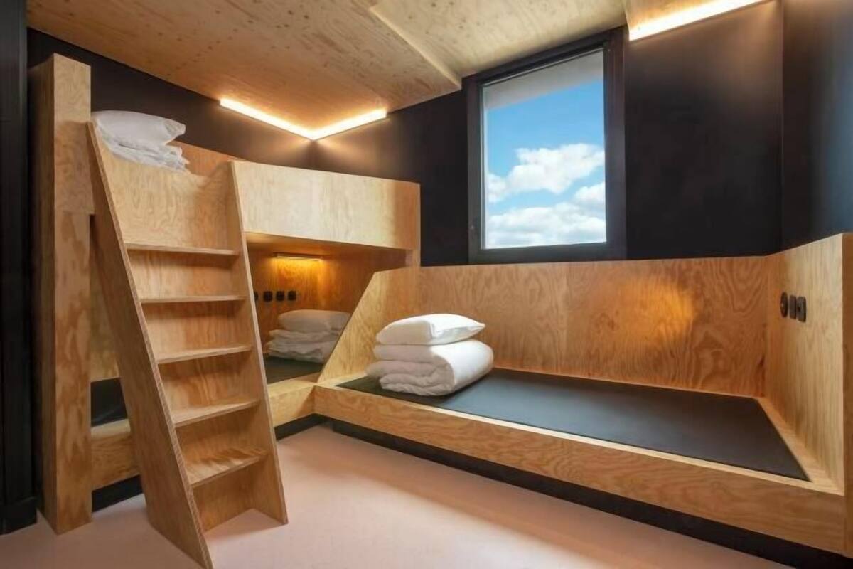 Una habitación moderna con una cama litera de madera, un banco empotrado con cojines y un tragaluz.