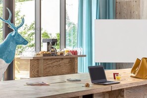 Un bureau en bois avec un ordinateur portable, une machine à café et un verre de jus d’orange. On peut voir un tableau blanc à l’arrière-plan.