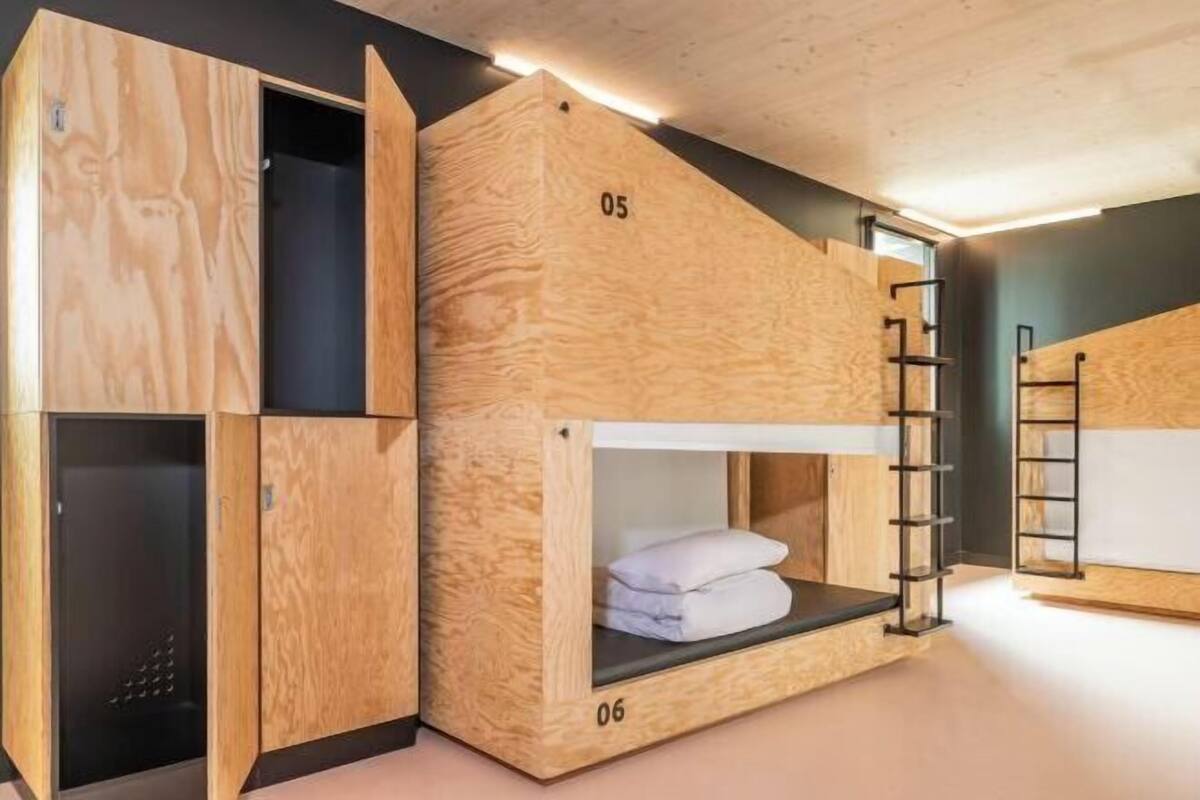 Una cama litera con estructura de madera, una escalera y un espacio pequeño cerrado debajo.