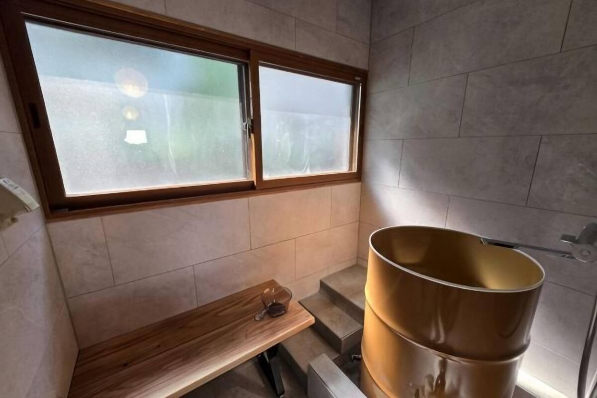 A bathroom with a window, a wooden bench, and a large metal container.