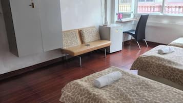 A hotel room with two beds, a desk, a chair, a bench, and a wardrobe.
