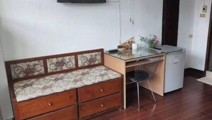 A small room with a wooden sofa with floral upholstery, a glass-top desk with a chair, and a small refrigerator. - Noy's House (Bangkok)