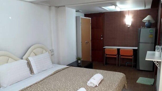 A hotel room with a bed, a desk, a chair, a refrigerator, and a small table with a lamp. - Noy's House (Bangkok)