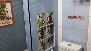 A bathroom with blue tiles, a toilet, and a shelf with decorative items. - Noy's House (Bangkok)