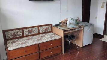 A room with a wooden bench with drawers, a small desk with a chair, and a refrigerator.