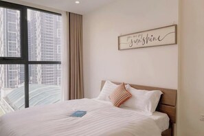 A hotel room with a large window, a bed with white bedding, a brown headboard, and a framed quote on the wall.