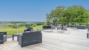 Une terrasse en bois, dotée de mobilier d’extérieur, d’un hamac et offrant une vue sur un paysage verdoyant.
