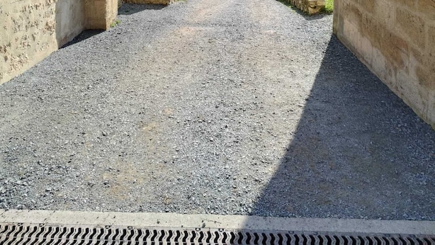 Un couloir en pierre, avec une entrée en arc, mène à un champ herbeux.