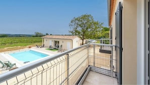 Un balcon avec une piscine, une petite maison et, au loin, un vignoble.