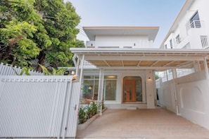 Una casa moderna de dos pisos con un porche cubierto, una cerca blanca y un árbol al fondo.