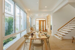Un vaste espace dédié à la salle à manger, avec une table et des chaises en bois, de grandes fenêtres et un escalier.