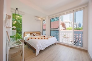 A bedroom with a bed, a desk, and a balcony with a view of buildings. - Bangkok four bedroom pool villa (Bangkok)